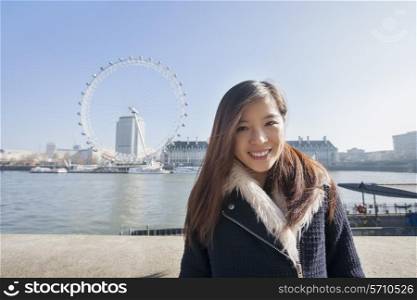 Portrait of happy young woman standing against London Eye at London; England; UK