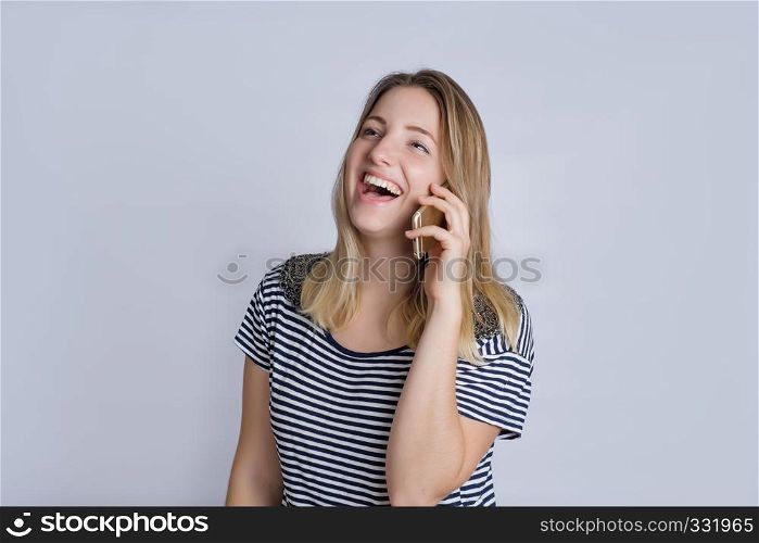 Portrait of happy young woman talking on phone in studio. Isolated on gray background