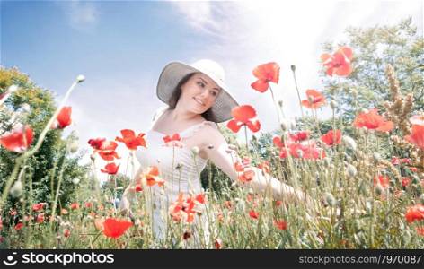 Portrait of Happy Young Woman Walking at the Meadow of Red Poppies in the Big White Hat in the Lovely Spring Day