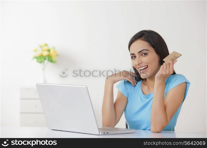 Portrait of happy young woman with credit card and laptop at home