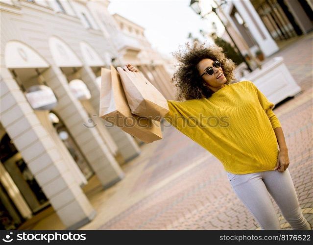 Portrait of happy young woman with  curly hair holding a lot of shopping bags with gifts outdoors