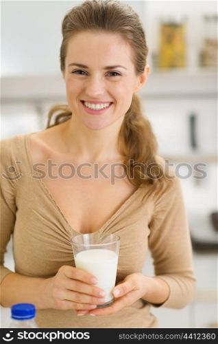 Portrait of happy young woman with glass of milk in kitchen