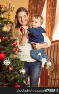 Portrait of happy young woman with her baby son decorating Christmas tree