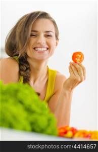 Portrait of happy young woman with tomato in kitchen