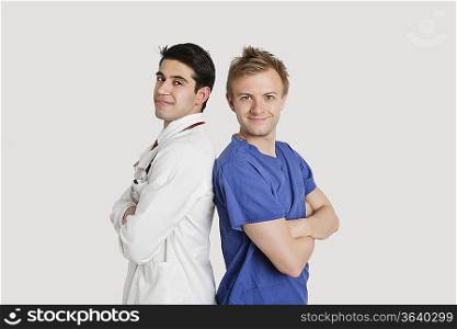 Portrait of healthcare professionals standing back to back over light gray background