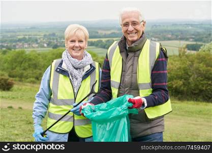 Portrait Of Helpful Senior Couple Collecting Litter In Countryside