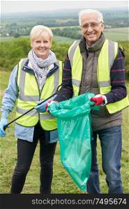 Portrait Of Helpful Senior Couple Collecting Litter In Countryside