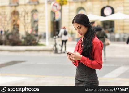 Portrait of hispanic businesswoman in urban background looking at her mobile phone