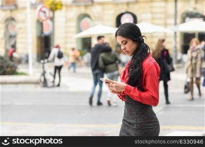 Portrait of hispanic bussinesswoman in urban background looking at her mobile phone
