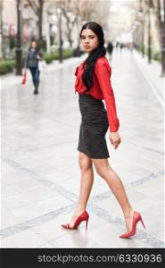 Portrait of hispanic bussinesswoman walking in urban background wearing red shirt and skirt