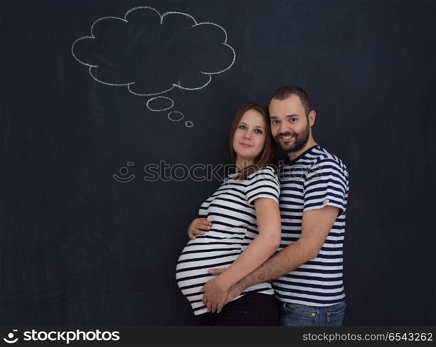 portrait of husband and pregnant wife posing against black chalk drawing board. pregnant couple posing against black chalk drawing board