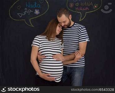 portrait of husband and pregnant wife posing against black chalk drawing board. pregnant couple posing against black chalk drawing board