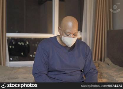 Portrait of ill old black american man, African person wearing a face mask for corona virus and health care concept in quarantine. Wearing medical mask on bed in bedroom. Stay home at late night.