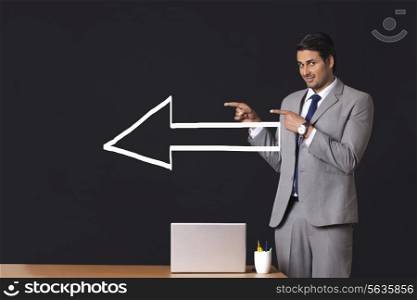 Portrait of Indian businessman with arrow sign pointing sideways in office
