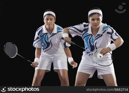 Portrait of Indian female partners playing badminton isolated over black background