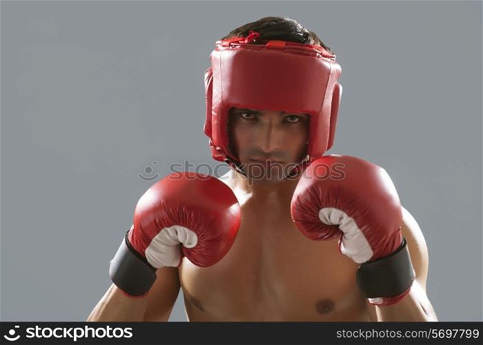 Portrait of Indian male boxer wearing gloves and head protector isolated over gray background