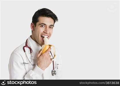 Portrait of Indian male doctor eating banana over white background