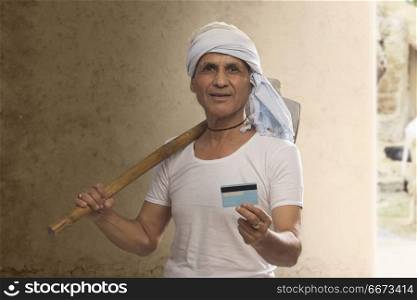 Portrait of Indian old farmer holding credit card and carrying hoe on his shoulder