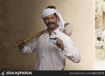 Portrait of Indian rural farmer holding credit card and carrying hoe on his shoulder