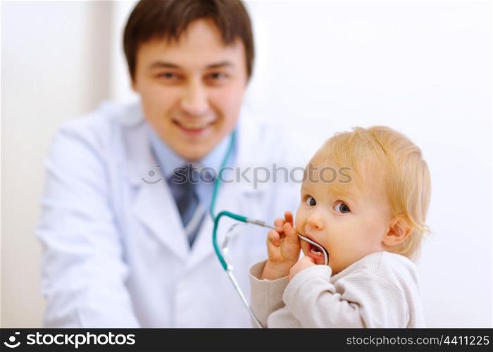 Portrait of interested baby with stethoscope and pediatric doctor in background&#xA;