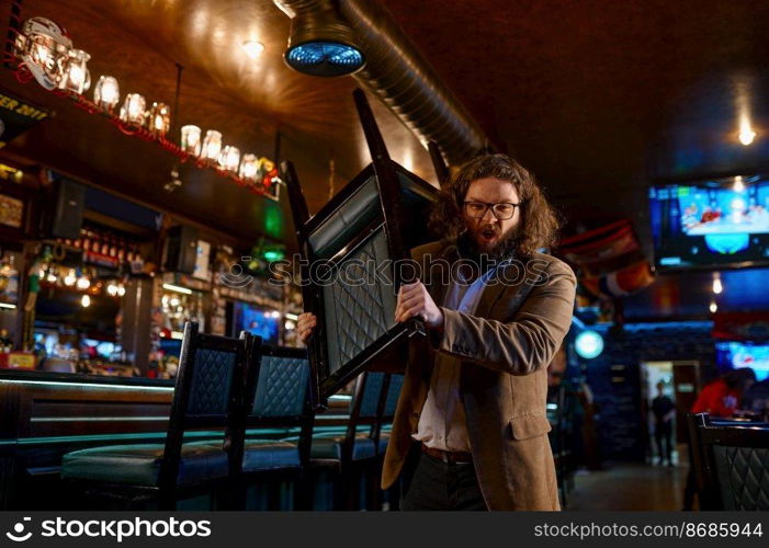 Portrait of irritated fury man with chair shouting and looking at camera. Sport bar interior. Irritated man with chair in sport bar