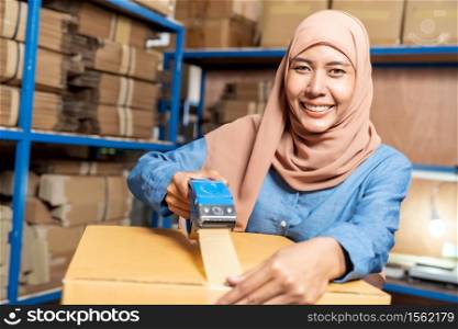 Portrait of Islam Muslim female asian warehouse worker packing and labelling on cardboard box in warehouse environment. Using in business warehouse logistic concept.
