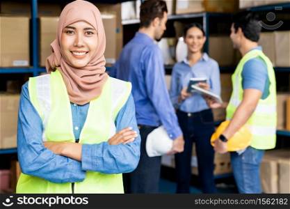 Portrait of Islam Muslim female warehouse worker crossed arm with her colleagues meeting in warehouse distribution center environment. For business warehouse inventory and logistic concept.