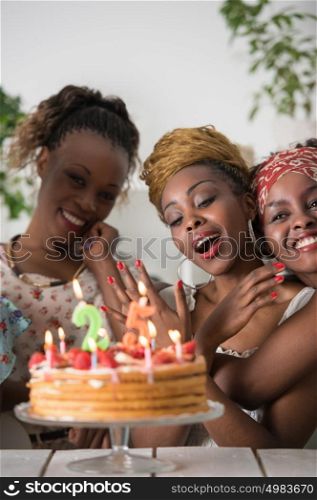 Portrait of joyful african girl looking at birthday cake surrounded by friends at party