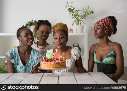 Portrait of joyful african girl looking at birthday cake surrounded by friends at party