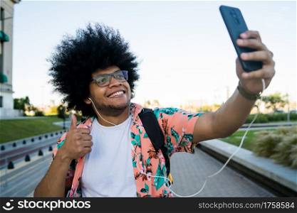 Portrait of latin man taking a selfie with his mobile phone while standing outdoors on the street. Urban concept.