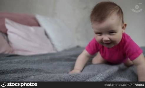 Portrait of laughing adorable infant child learning to crawl on bed. Closeup. Cute baby girl crawling and smiling. Slow motion.