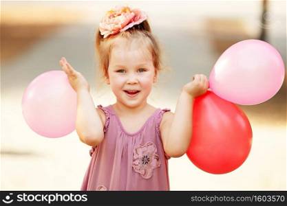 Portrait of laughing and playing little girl holding colorful balloons. Positive emitions. Happy child.