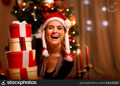 Portrait of laughing woman near Christmas tree looking out from pile of present boxes &#xA;