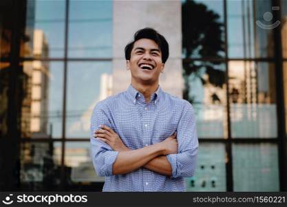 Portrait of Laughing Young Asian Businessman in the City. Crossed Arms and looking away. a Happy Friendly Man