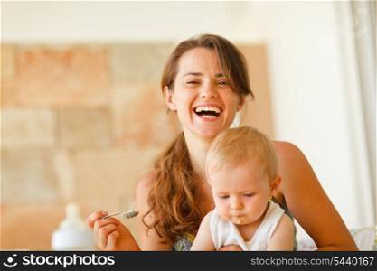 Portrait of laughing young mother feeding baby&#xA;