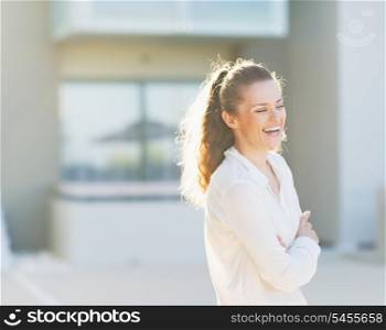 Portrait of laughing young woman standing in front of house building