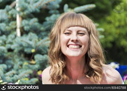 Portrait of laughing young woman with blond hair on summer background