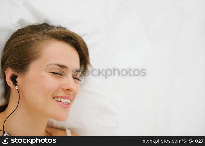 Portrait of laying on bed girl in headphones listening music. Upper view