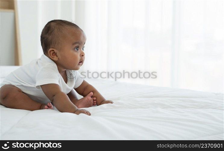 Portrait of little adorable African newborn baby sitting on bed and looking with bright eyes and trying to crawl on her own at home.  Development and growth of children concept. Copy space
