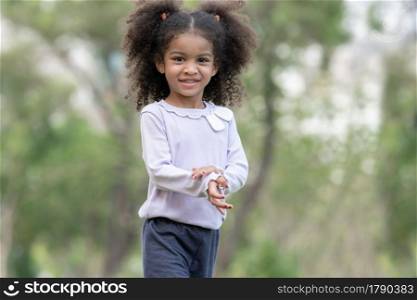 Portrait of little African kid girl with twin tails hair smiling and looking at camera at green park
