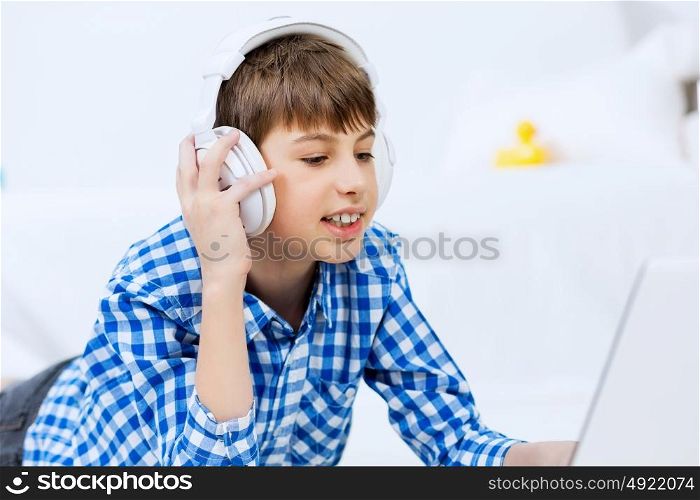 Portrait of little boy listening music from laptop through headphones while lying on hardwood floor. Boy of school age listening music from laptop through headphones while lying on floor