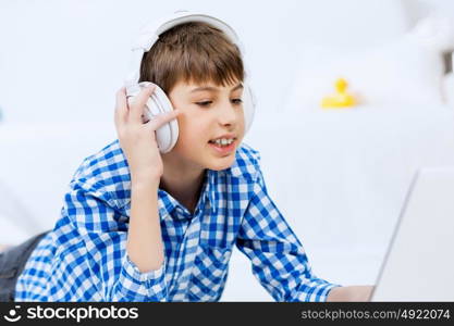 Portrait of little boy listening music from laptop through headphones while lying on hardwood floor. Boy of school age listening music from laptop through headphones while lying on floor