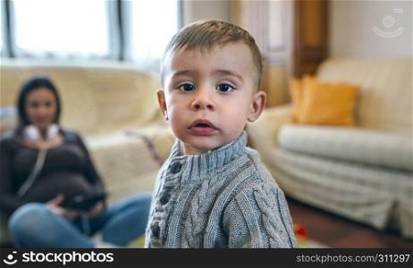 Portrait of little boy looking at camera with his pregnant mother sitting in the background. Little boy looking at camera with his pregnant mother sitting in background
