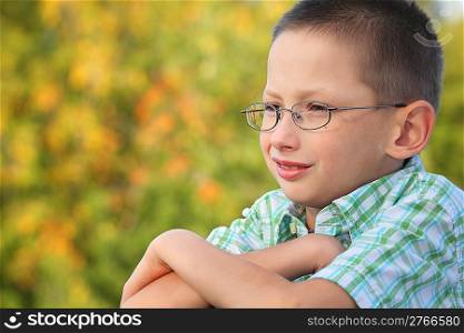 portrait of little boy with arms across in early fall park. he is looking away.