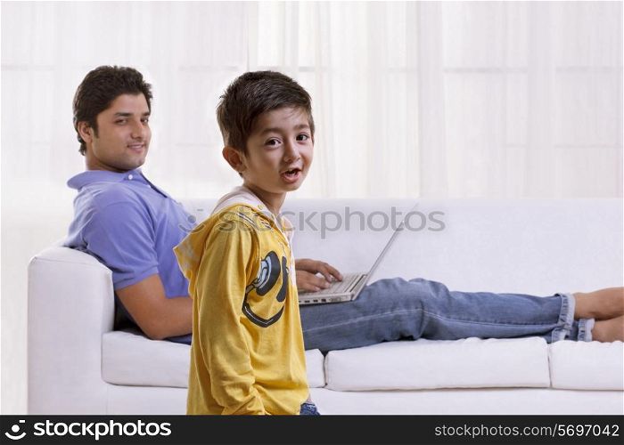 Portrait of little boy with father using laptop in the background