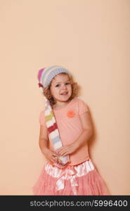 Portrait of little curly girl in the winter colorful hat posing for photo. Fashion girl portrait