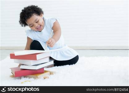 Portrait of Little cute African chubby kid girl use left hand writing on paper on stack of textbooks with toys and sitting on floor at home. Child education concept. White background. Copy space