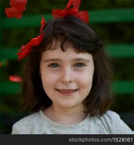 Portrait of little girl among red petals on a dark green background, square image