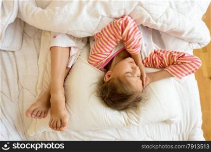 Portrait of little girl and sisters feet on pillow at bed