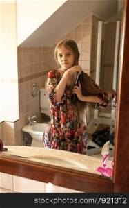 Portrait of little girl combing hair at bathroom